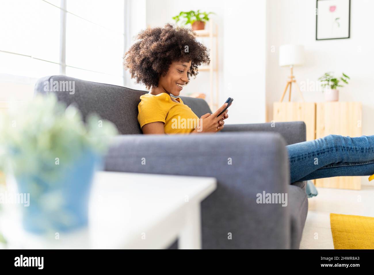 Felice giovane donna messaggi di testo tramite smartphone a casa Foto Stock
