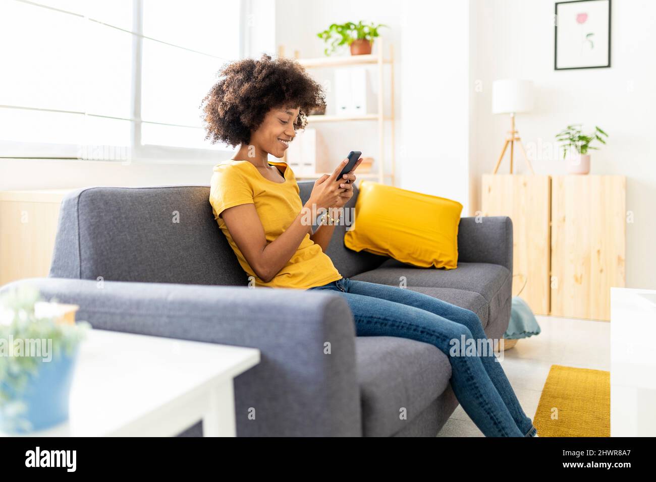 Messaggio di testo donna felice tramite telefono cellulare sul divano a casa Foto Stock
