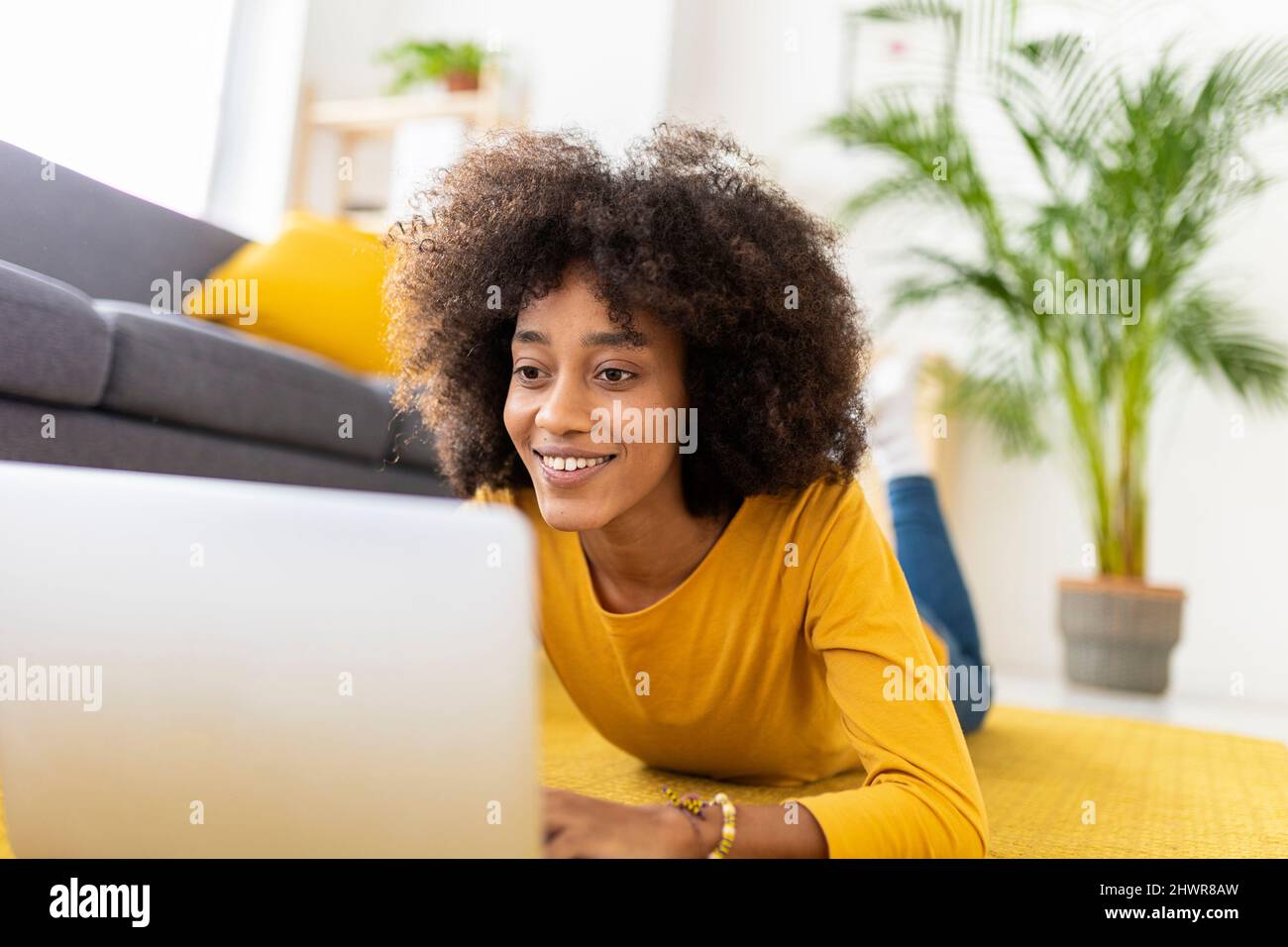 Donna felice che usa un computer portatile sdraiato in salotto a casa Foto Stock