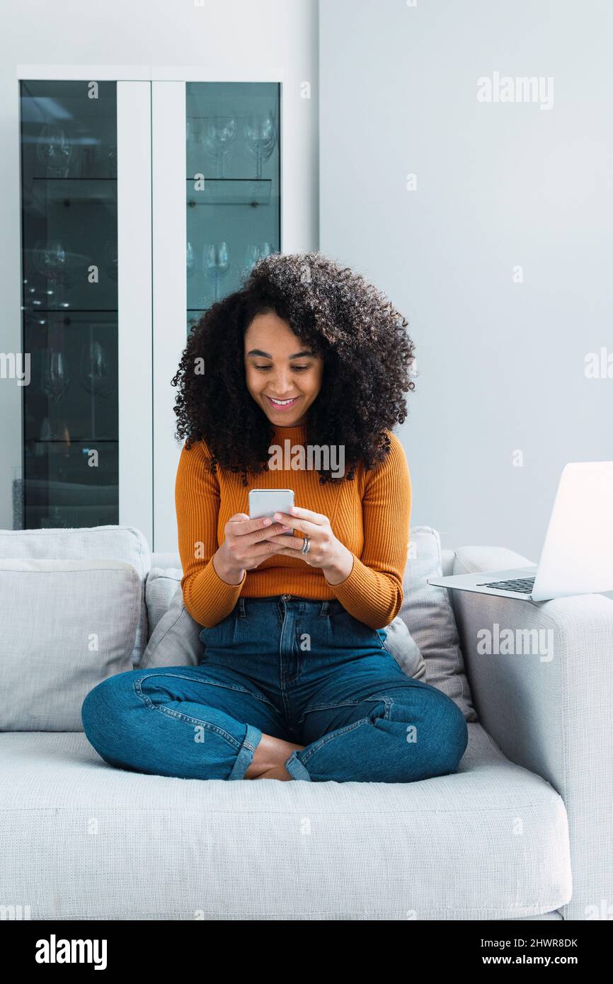 Messaggi di testo per donna sorridente tramite telefono cellulare a casa Foto Stock