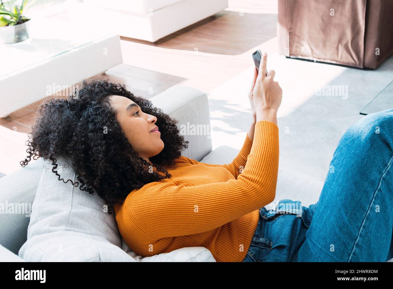 Donna che utilizza il telefono cellulare sdraiato sul divano in soggiorno Foto Stock