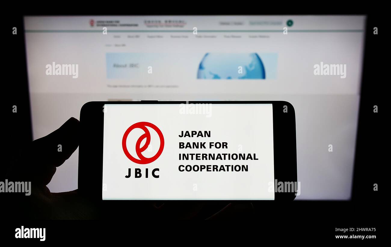 Persona che tiene uno smartphone con il logo della Japan Bank for International Cooperation (JBIC) sullo schermo di fronte al sito Web. Mettere a fuoco sul display del telefono. Foto Stock