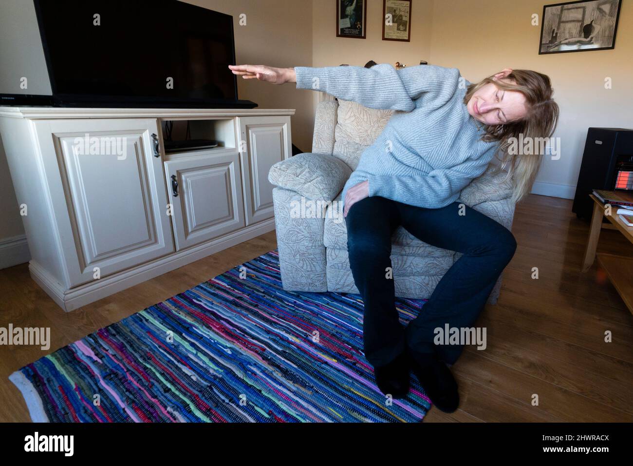 Donna bionda alta che fa mattina esercizi di stretching in poltrona Foto Stock