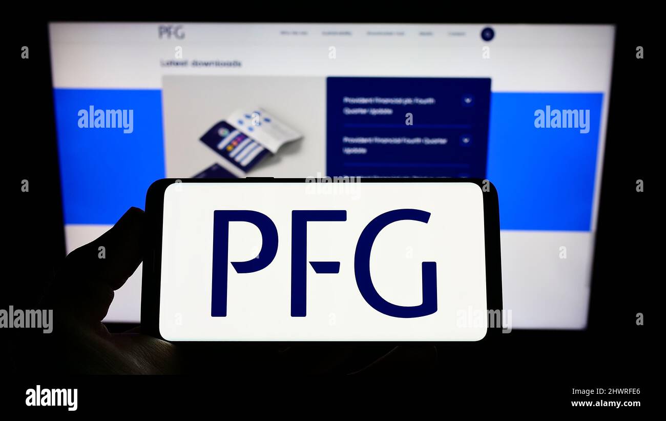 Persona che tiene il cellulare con il logo della società britannica Provident Financial plc (PFG) sullo schermo di fronte alla pagina web. Mettere a fuoco sul display del telefono. Foto Stock