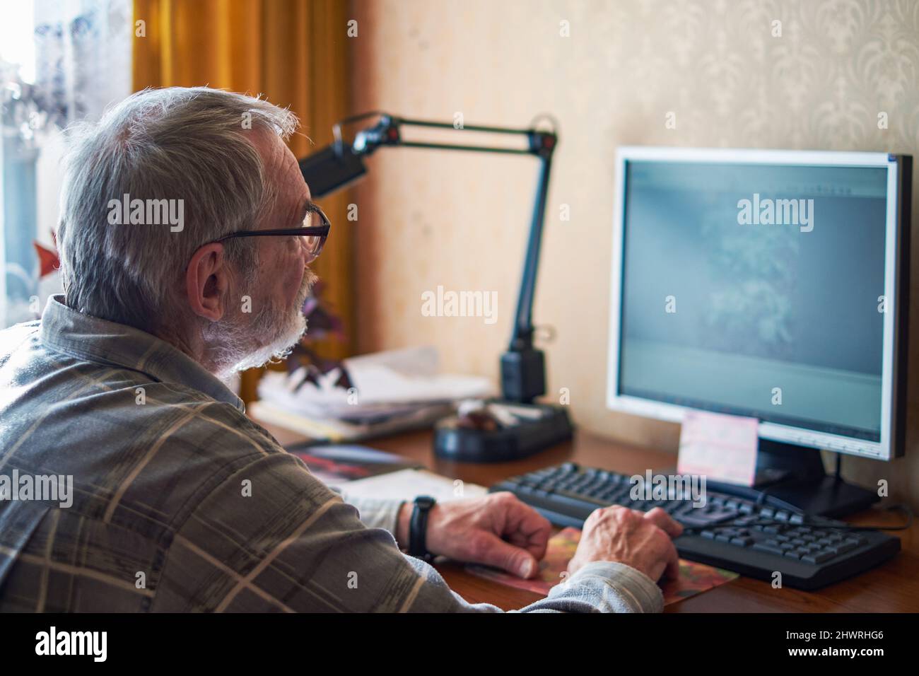Un uomo anziano, 70+, lavora a casa in un computer Foto Stock