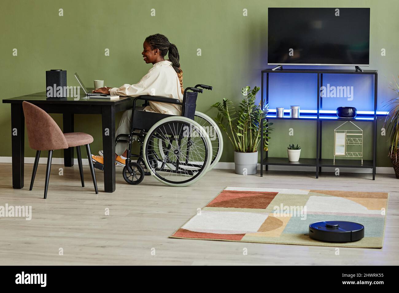 Ritratto della giovane afroamericana con sedia a rotelle mentre lavora in ufficio con dispositivi smart home accessibili Foto Stock