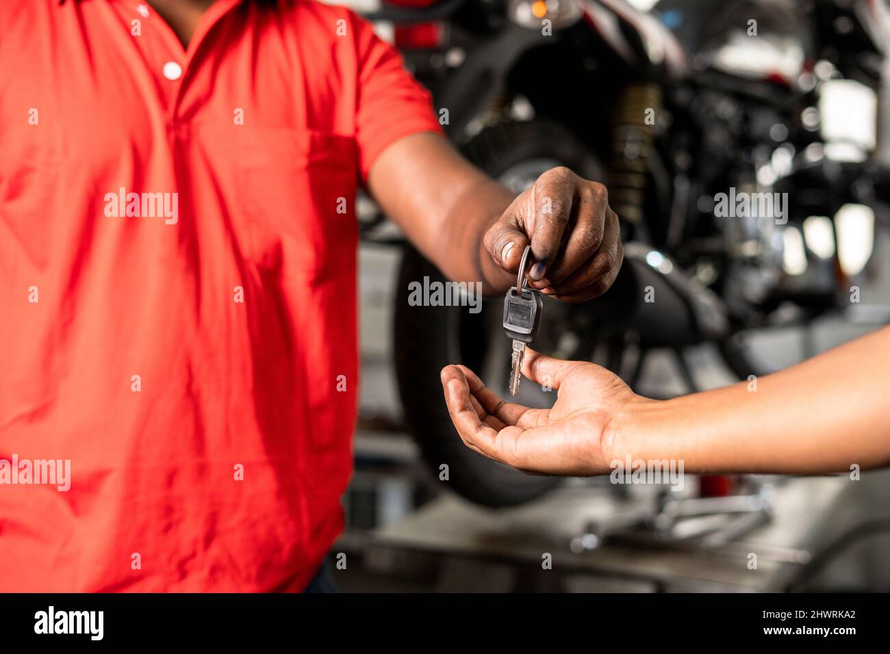 Primo piano delle mani del meccanico della motocicletta che danno la chiave del motobike al cliente dopo il servizio di manutenzione al garage - concetto di riuscita riparazione di completamento Foto Stock