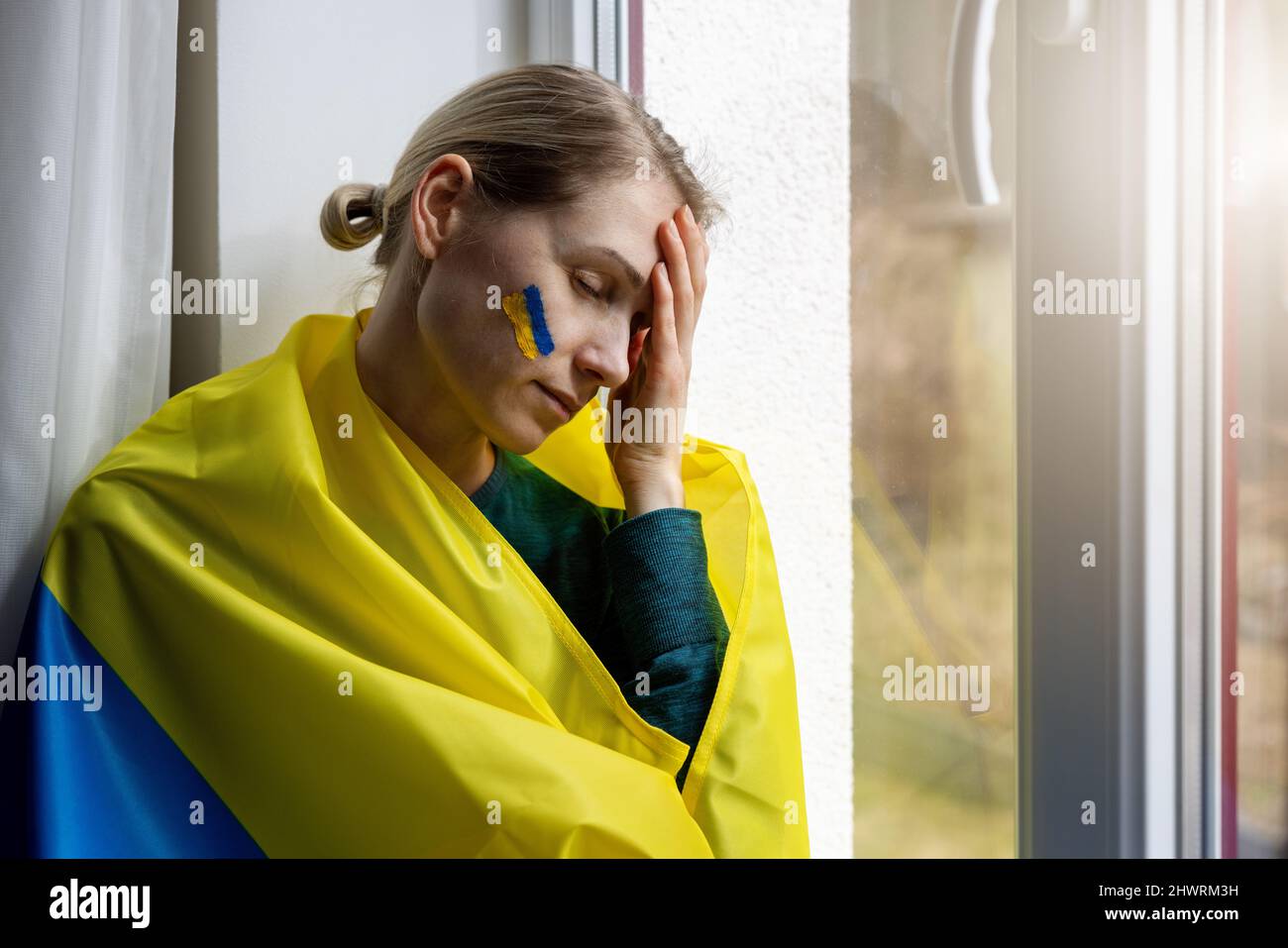 triste donna preoccupata con bandiera ucraina sedersi sul davanzale. solidarietà e empatia concetto Foto Stock