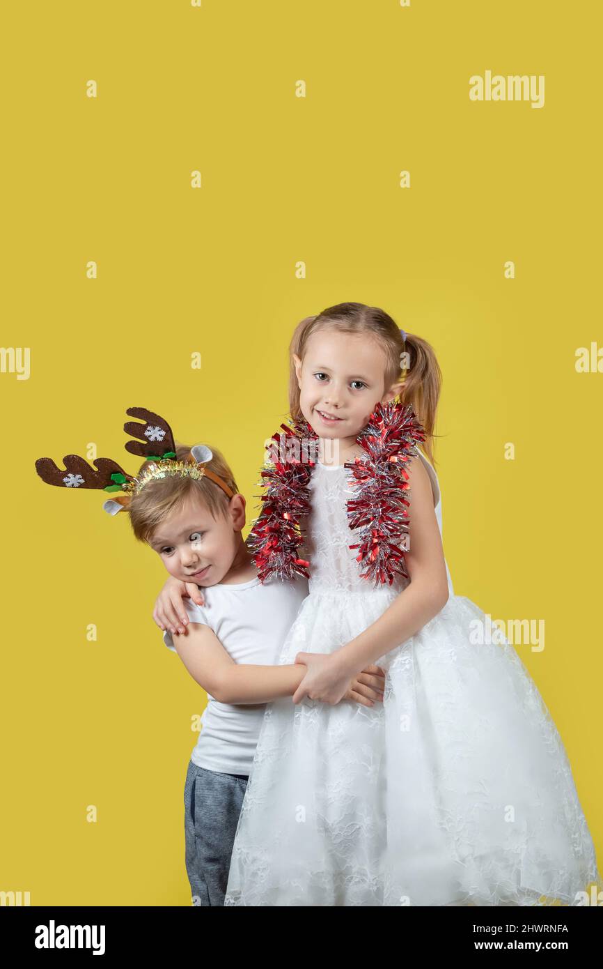 Ritratto di bambini carini in costume da renna di natale e bel vestito guardando la macchina fotografica su uno sfondo giallo, preparando per il nuovo Yea Foto Stock