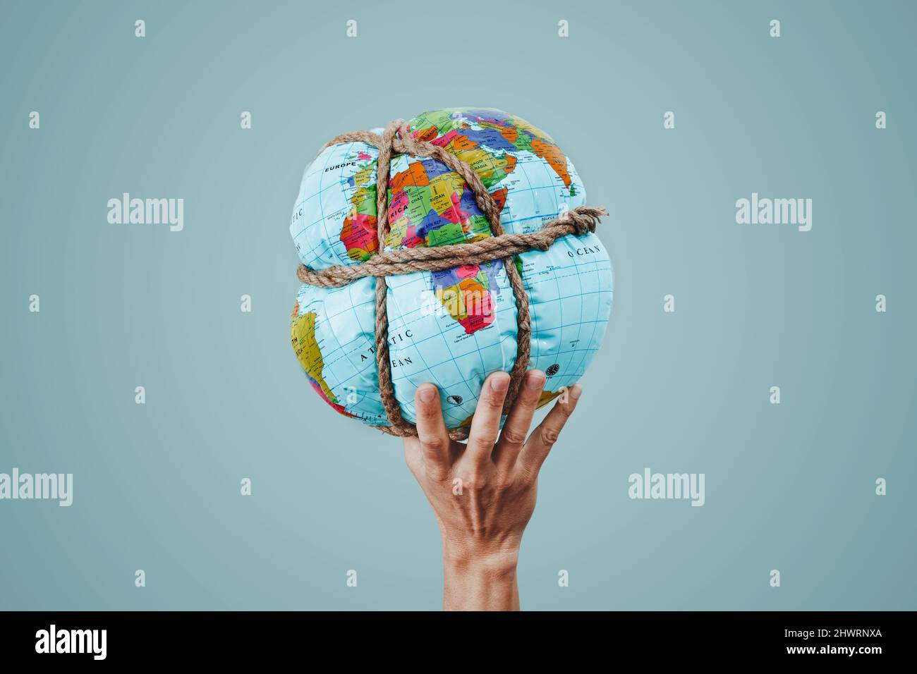 un giovane uomo tiene un globo di terra strettamente legato con corda in mano, su sfondo azzurro pallido Foto Stock