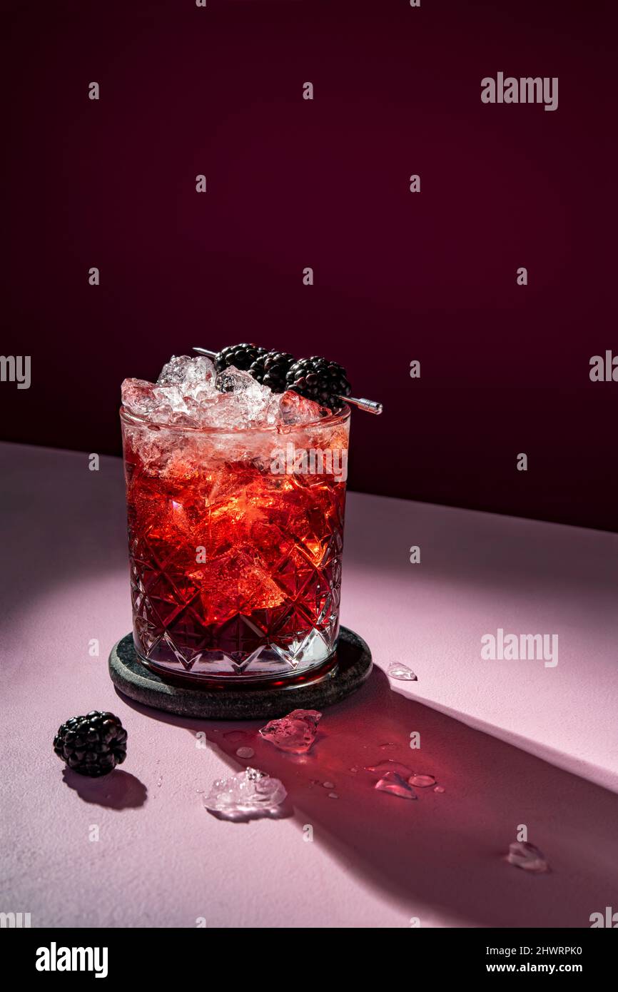 Cocktail estivo freddo drink con ghiaccio guarnito con mora su sfondo violetto Foto Stock