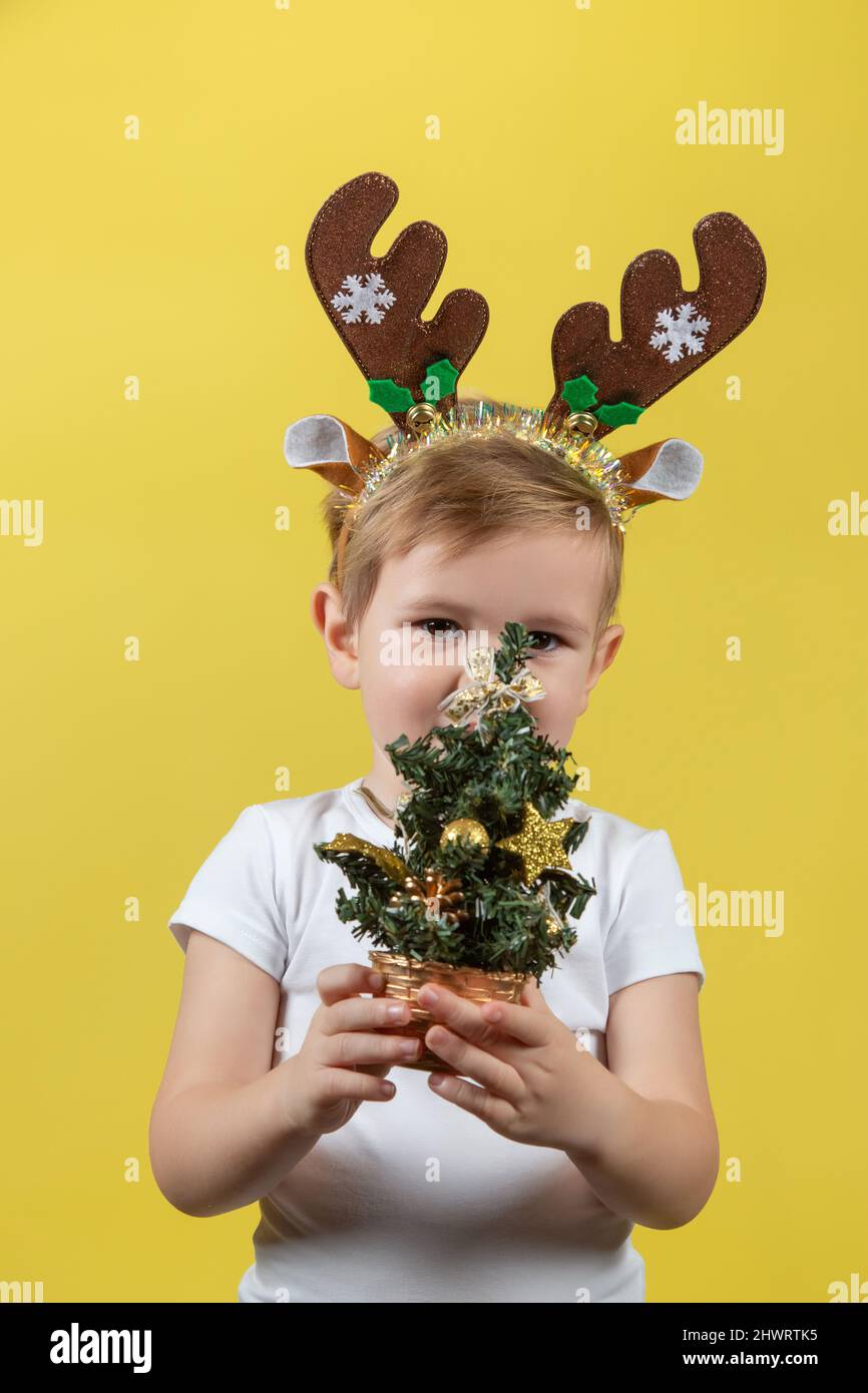 Felice ragazzo divertente bambino in rosso costume di renna di Natale con albero decorativo di natale su sfondo giallo Foto Stock