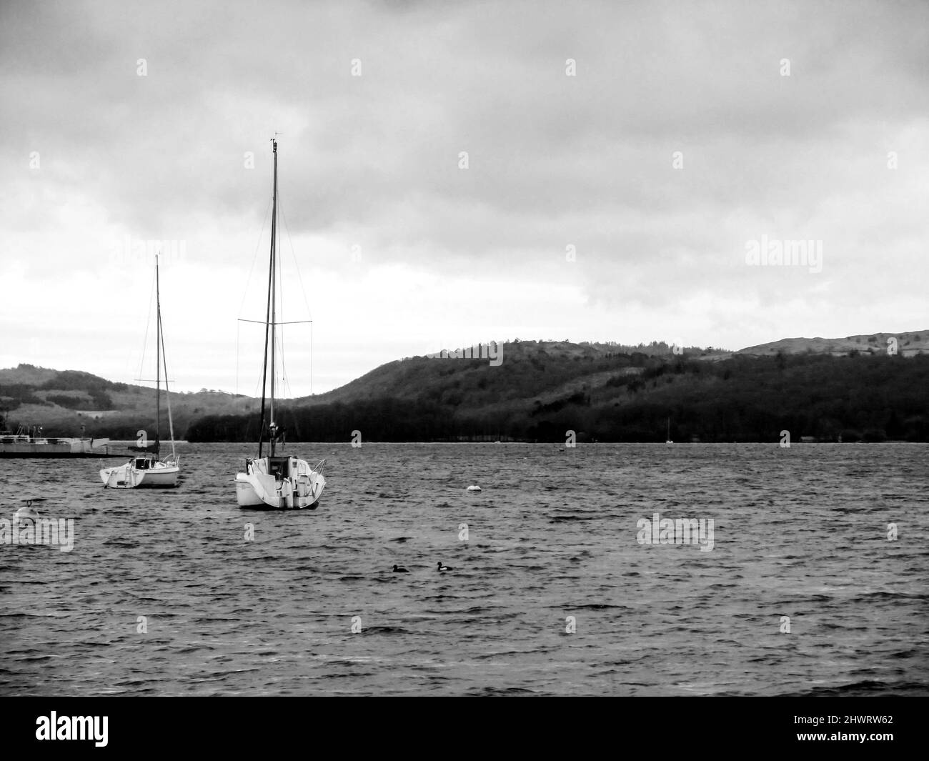 Due barche a vela ormeggiate sul lago Windermere nel Lake District, Regno Unito, in una giornata fredda e piovosa in bianco e nero Foto Stock