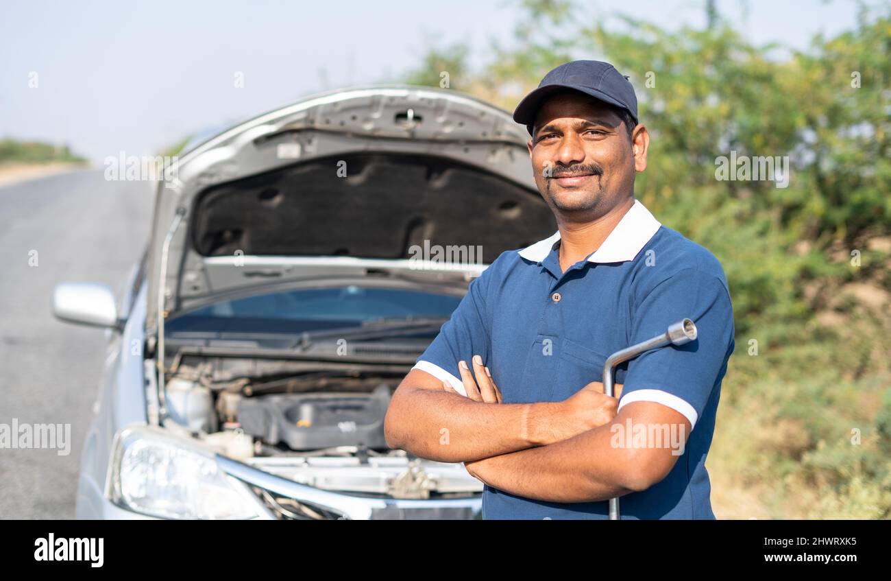 Portriat ha girato sorridendo meccanico auto stading di fronte al borken sulla strada guardando la macchina fotografica - concetto di servizio di auto mobile o di supporto e. Foto Stock