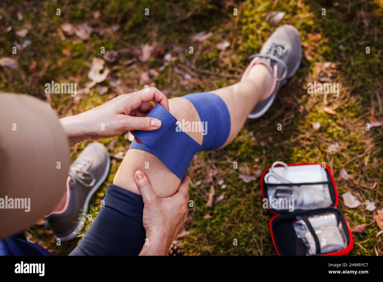 Fissazione della pioggia del ginocchio durante le escursioni. Donna ferita con fasciatura elastica del kit di pronto soccorso Foto Stock