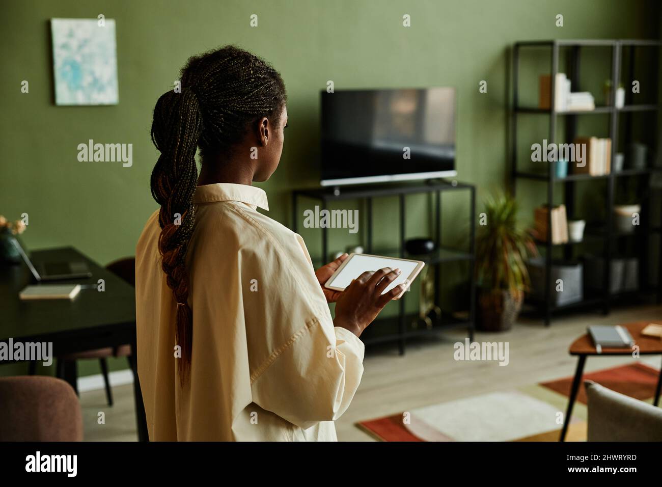 Vista laterale ritratto della giovane donna nera che tiene un tablet con schermo vuoto durante il funzionamento di dispositivi domestici intelligenti, spazio di copia Foto Stock