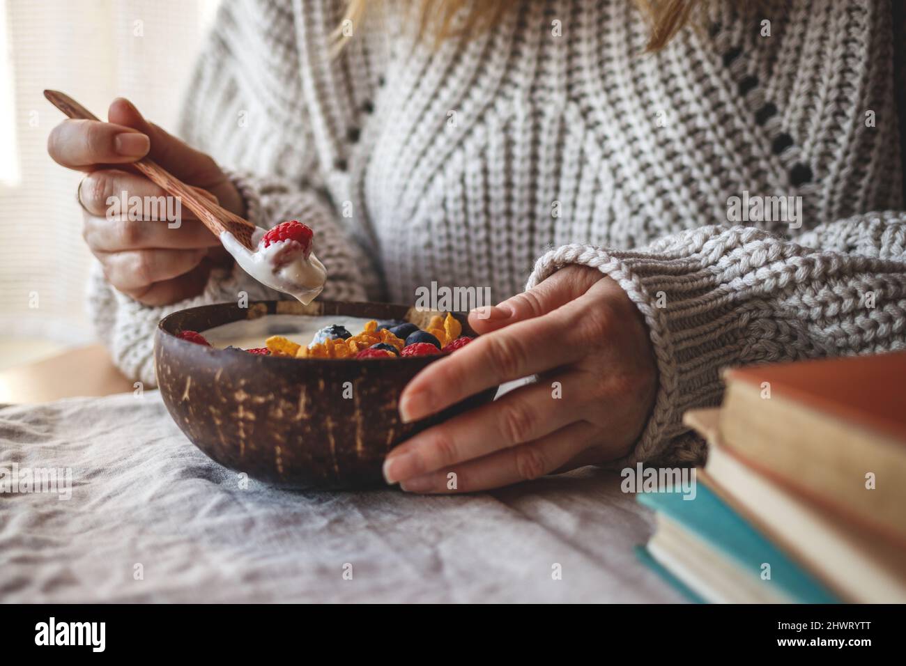 Donna che mangia una sana colazione dalla ciotola di cocco. Yogurt con fiocchi di mais e frutti di bosco Foto Stock