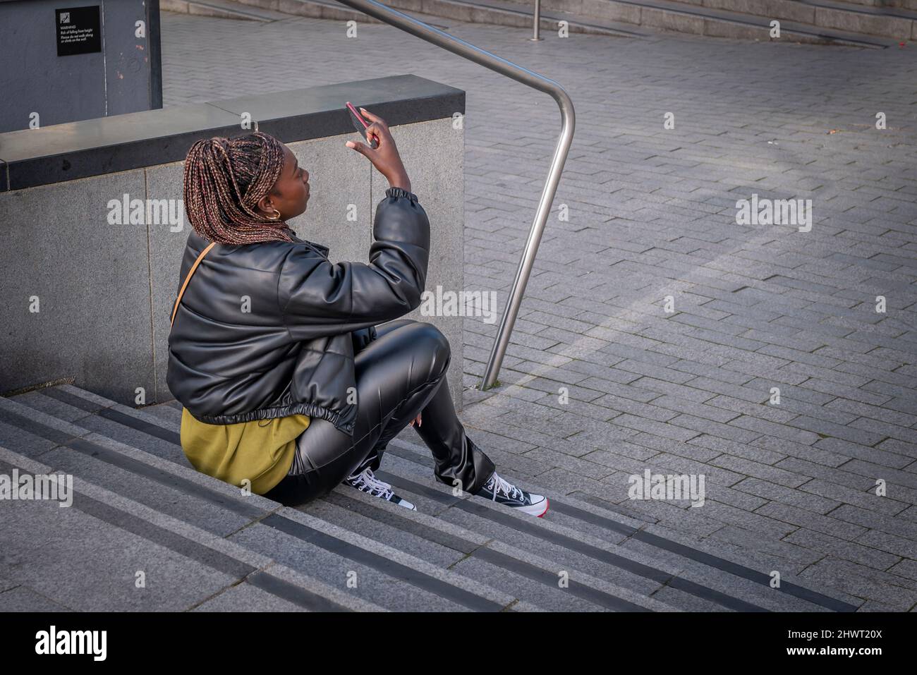 Una giovane donna con trecce lunghe che guarda il suo smartphone. Foto Stock