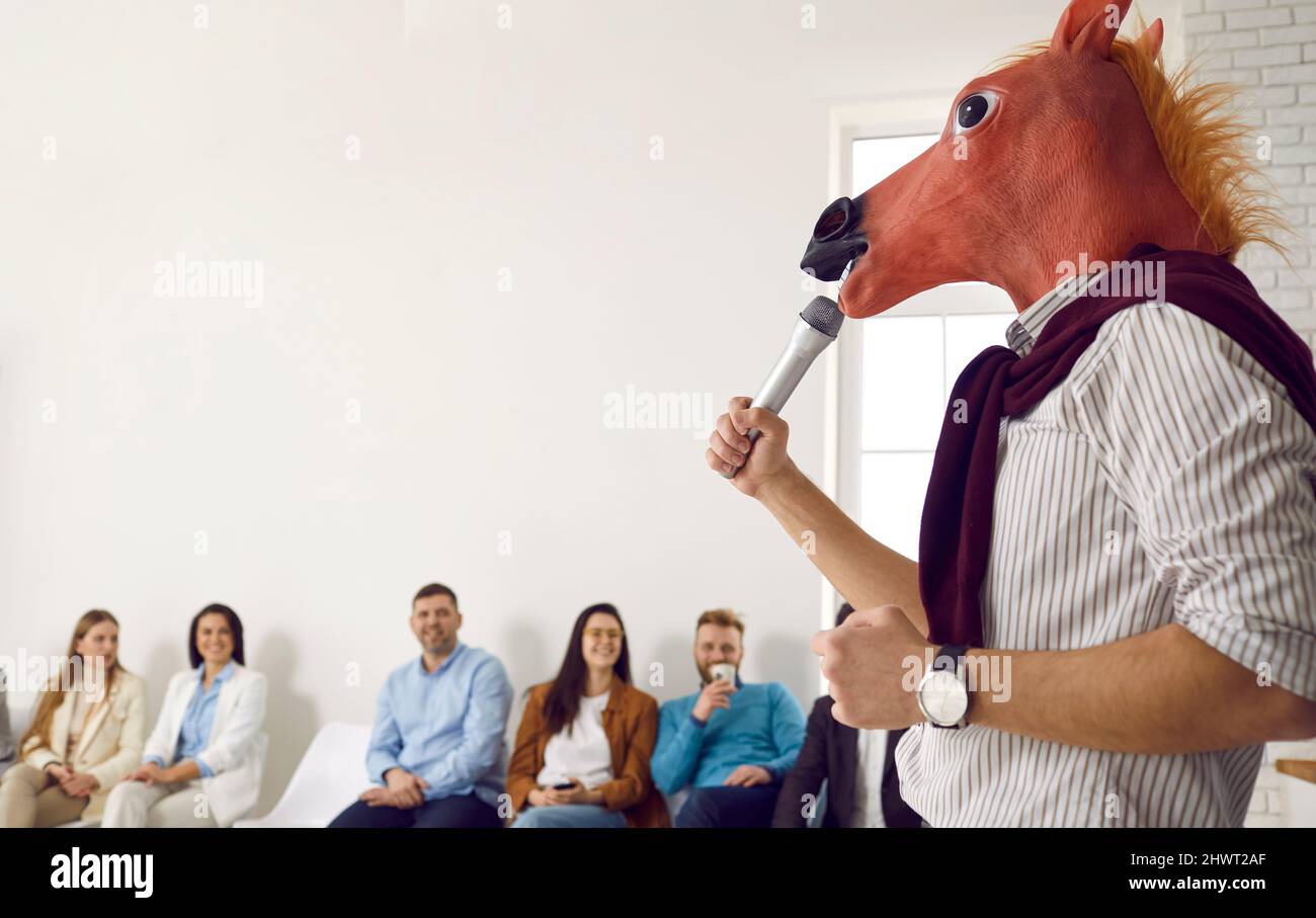 Altoparlante di affari nella maschera di cavallo che fa la presentazione divertente davanti al pubblico felice Foto Stock