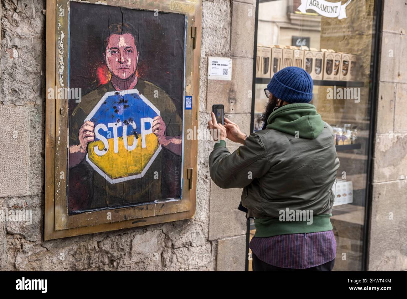 Barcellona, Spagna. 07th Mar 2022. Una persona è vista scattare una foto del collage che raffigura il presidente ucraino Zelensky che chiede la fine dell'invasione russa è visto in Plaza de Sant Jaume.l'artista italiano TvBoy residente a Barcellona mette una rappresentazione del collage del presidente ucraino Volodímir Zelensky che chiede la fine di L'occupazione russa in uno degli accessi alla Plaza Sant Jaume. Credit: SOPA Images Limited/Alamy Live News Foto Stock