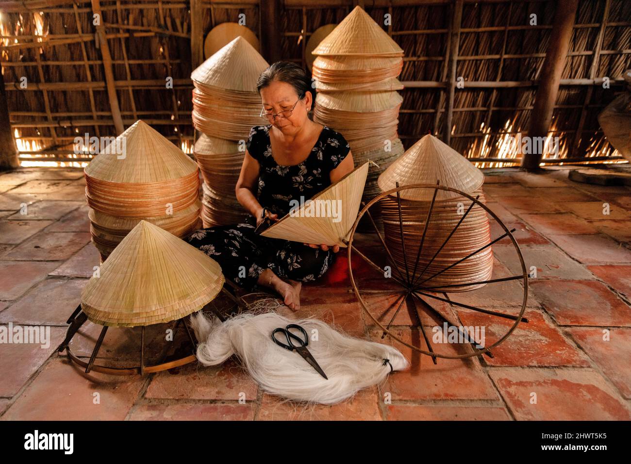 vecchia donna vietnamita che fa un cappello conico tradizionale a casa sua Foto Stock