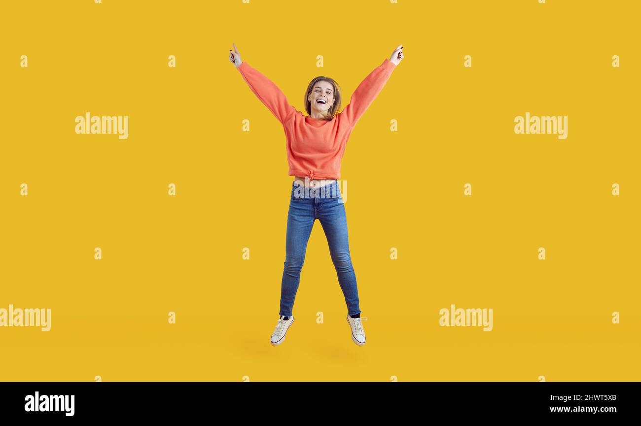 Felice allegra giovane donna eccitata in abiti casual che saltano per la gioia in studio Foto Stock