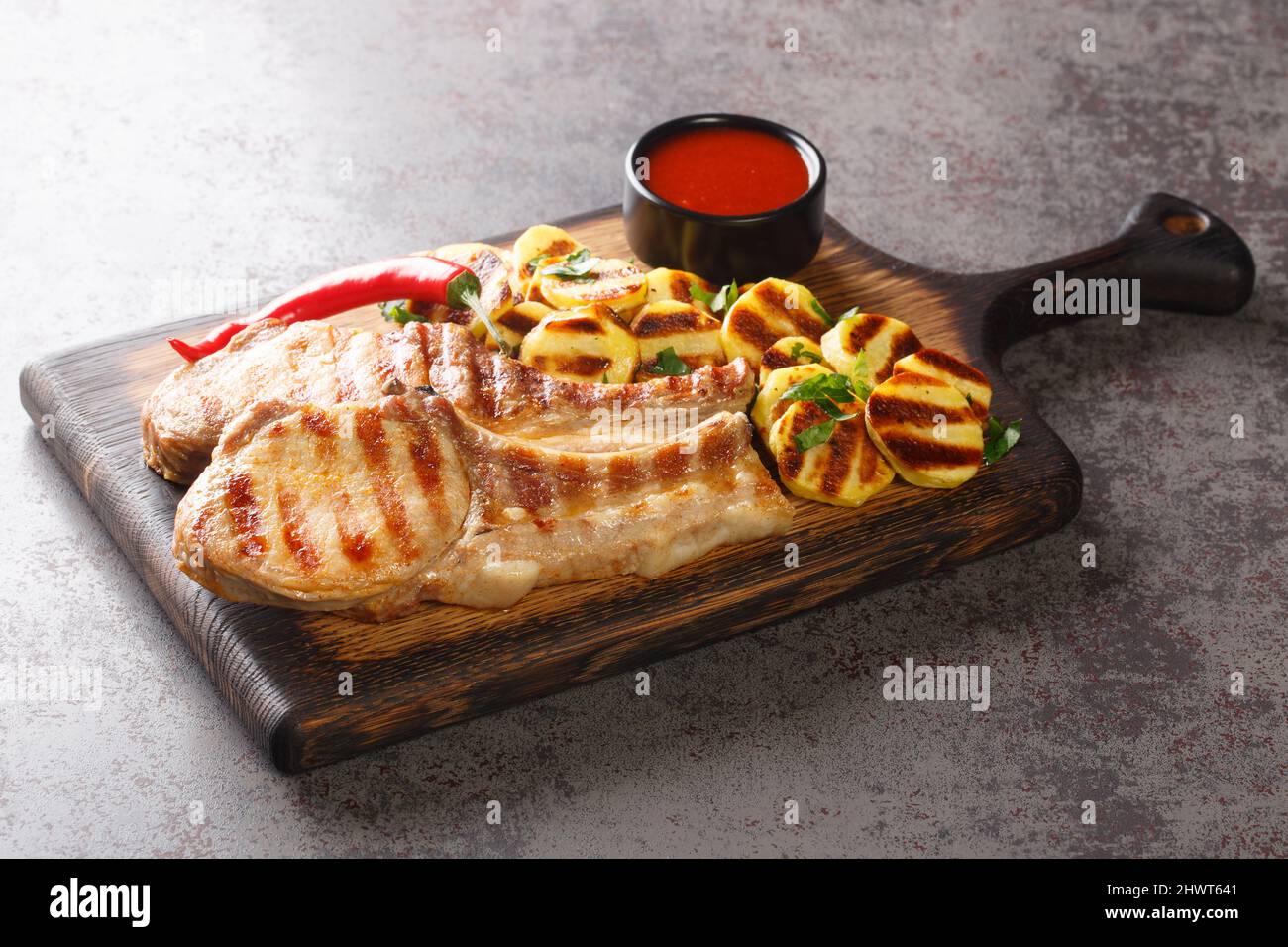 Braciole di maiale alla griglia fatte in casa e patate alla griglia pronte da mangiare su un bordo di legno sul primo piano del tavolo. Orizzontale Foto Stock