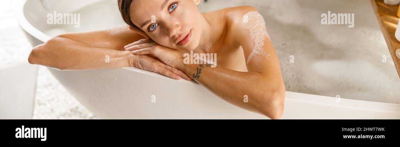 Bella giovane donna che si sente stanca, appoggiata sul lato della vasca da bagno, mentre si fa il bagno rilassante al centro benessere Foto Stock