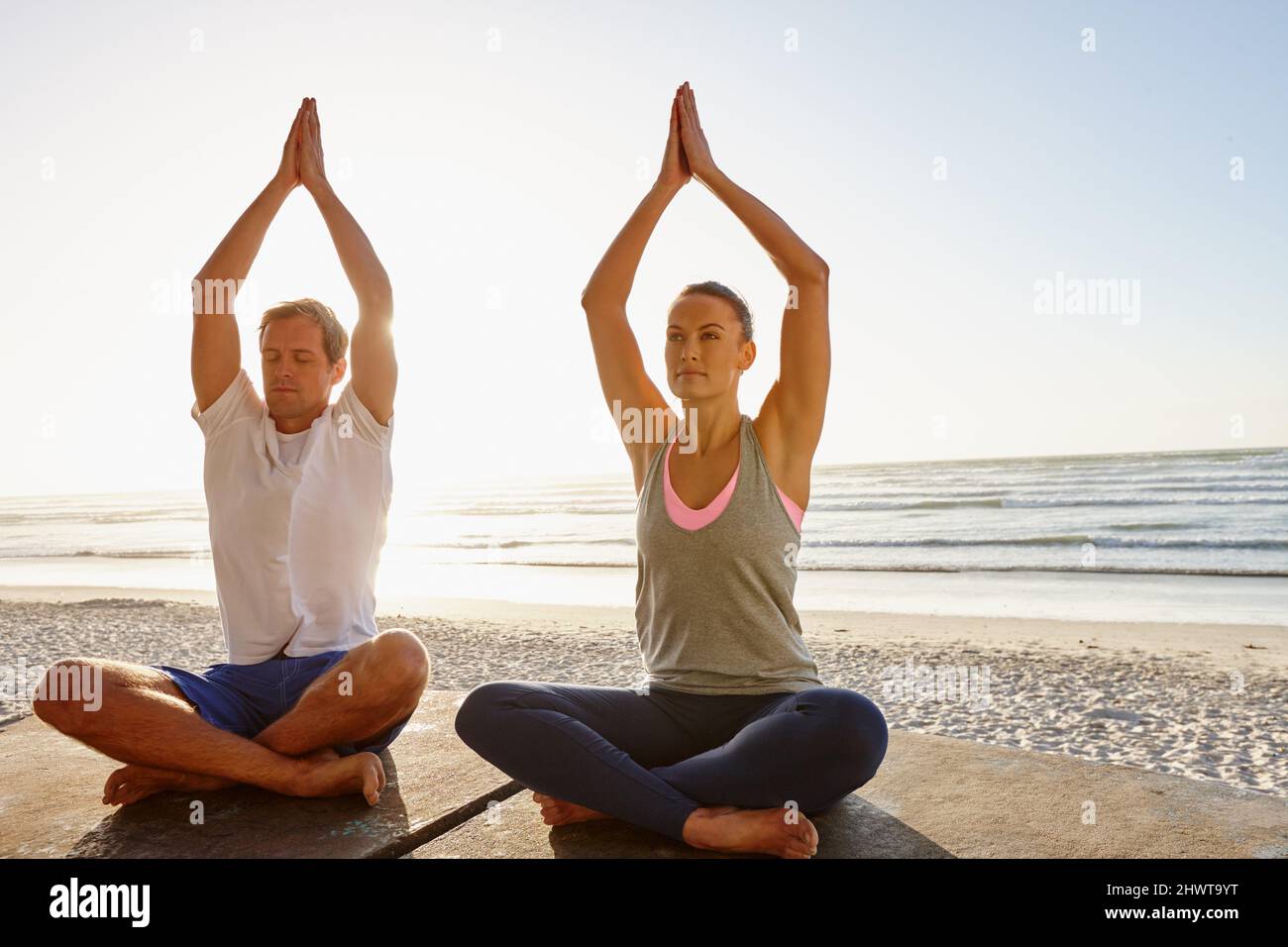 Il theyre che conduce uno stile di vita equilibrato. Scatto di una coppia che fa yoga in spiaggia al tramonto. Foto Stock