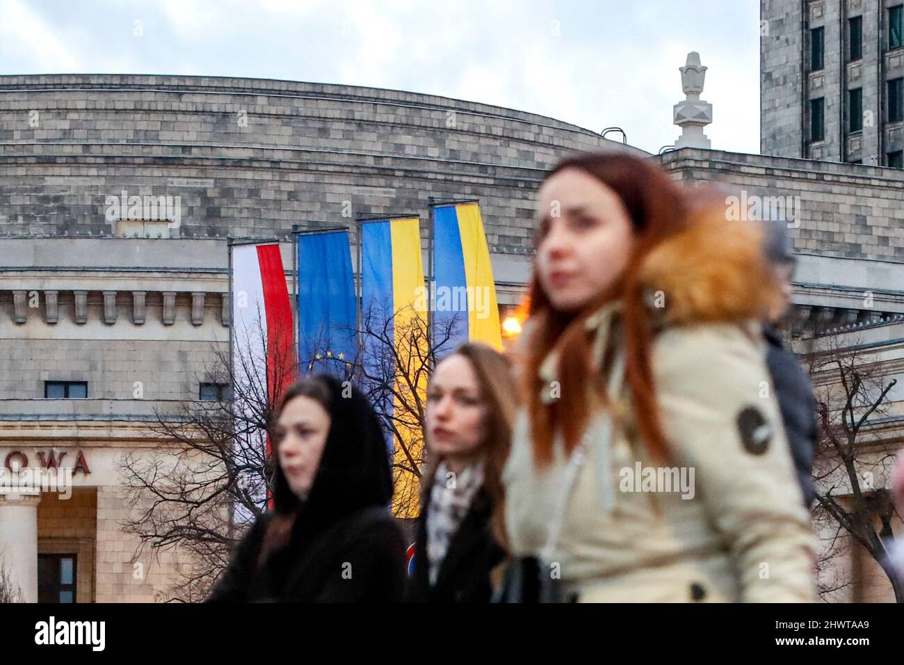 Varsavia, Varsavia, Polonia. 7th Mar 2022. La gente passa accanto alla Sala dei Congressi del Palazzo della Cultura e della Scienza, dove vengono erette bandiere di Polonia, Ucraina e Unione europea (UE), a seguito dell'invasione russa dell'Ucraina. Milioni di rifugiati fuggono dall'Ucraina verso paesi vicini, tra cui Polonia, Lituania, Germania e Paesi Bassi, mentre gli attacchi militari russi continuano contro i civili. (Credit Image: © Daniel Ceng Shou-Yi/ZUMA Press Wire) Foto Stock