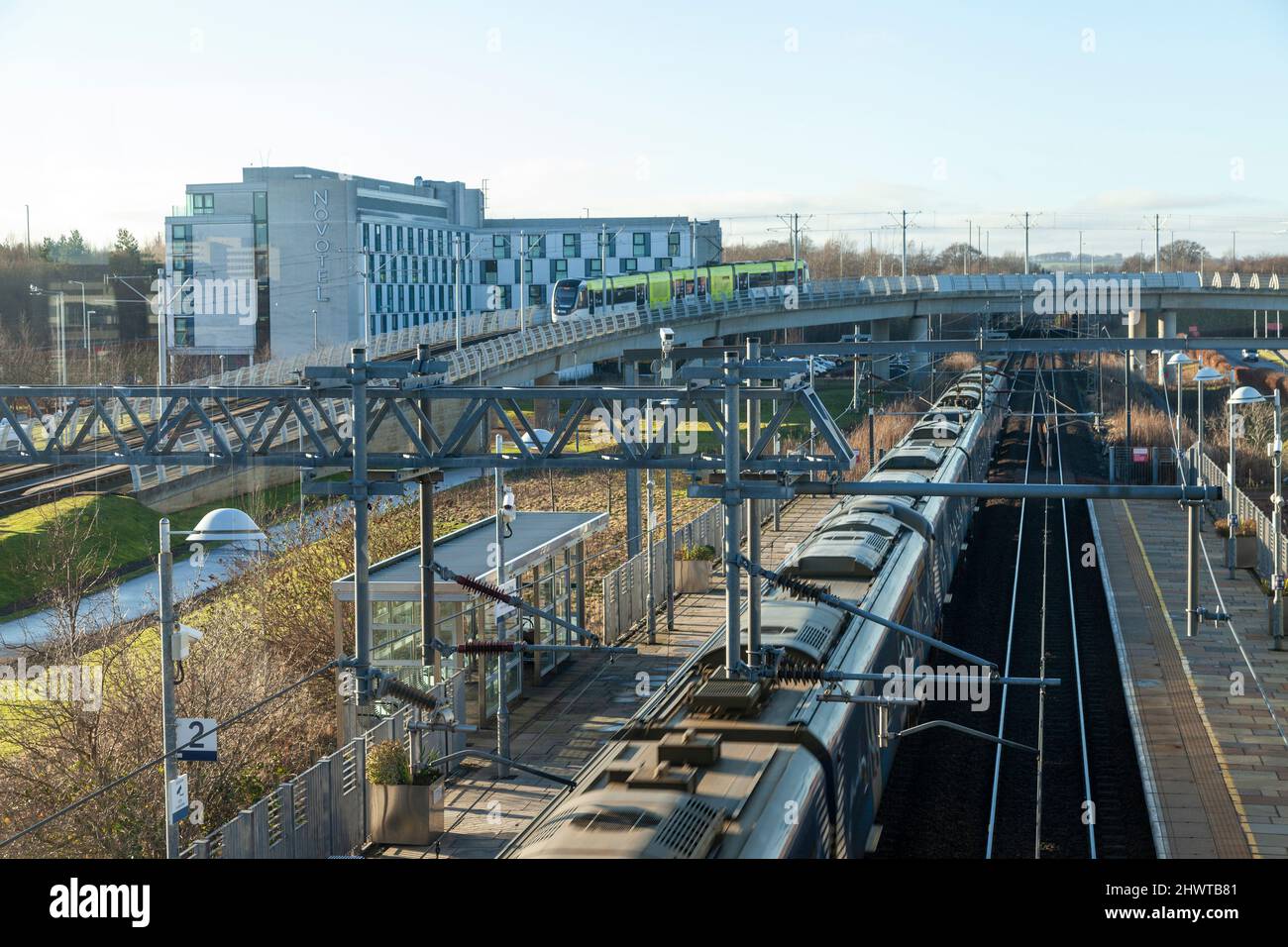 La vista dalla stazione ferroviaria di Edinburgh Park di un treno nella stazione e di un tram sul cavalcavia, Edimburgo Foto Stock