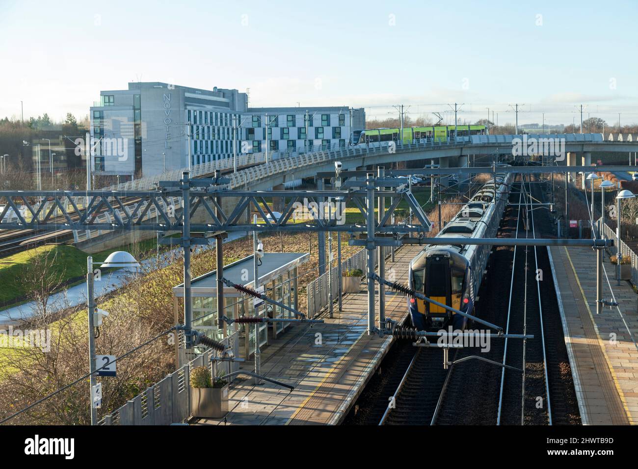 La vista dalla stazione ferroviaria di Edinburgh Park di un treno nella stazione e di un tram sul cavalcavia, Edimburgo Foto Stock