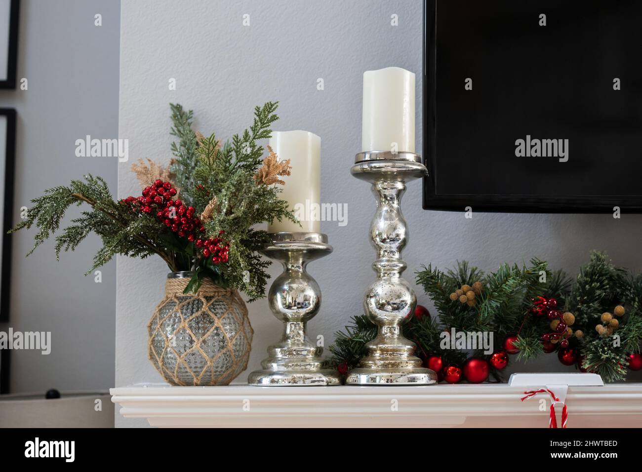 Un mantello natalizio bianco decorato con ghirlande di pino, candelabri d'argento con candele e un televisore Foto Stock