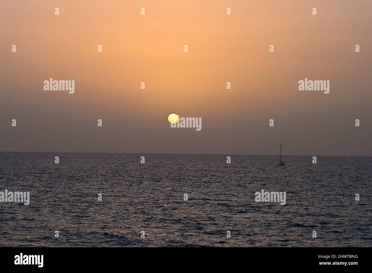 Un tranquillo tramonto lontano in un caldo giorno di febbraio sopra l'Oceano Atlantico al tramonto con una barca a vela che attraversa l'orizzonte Foto Stock