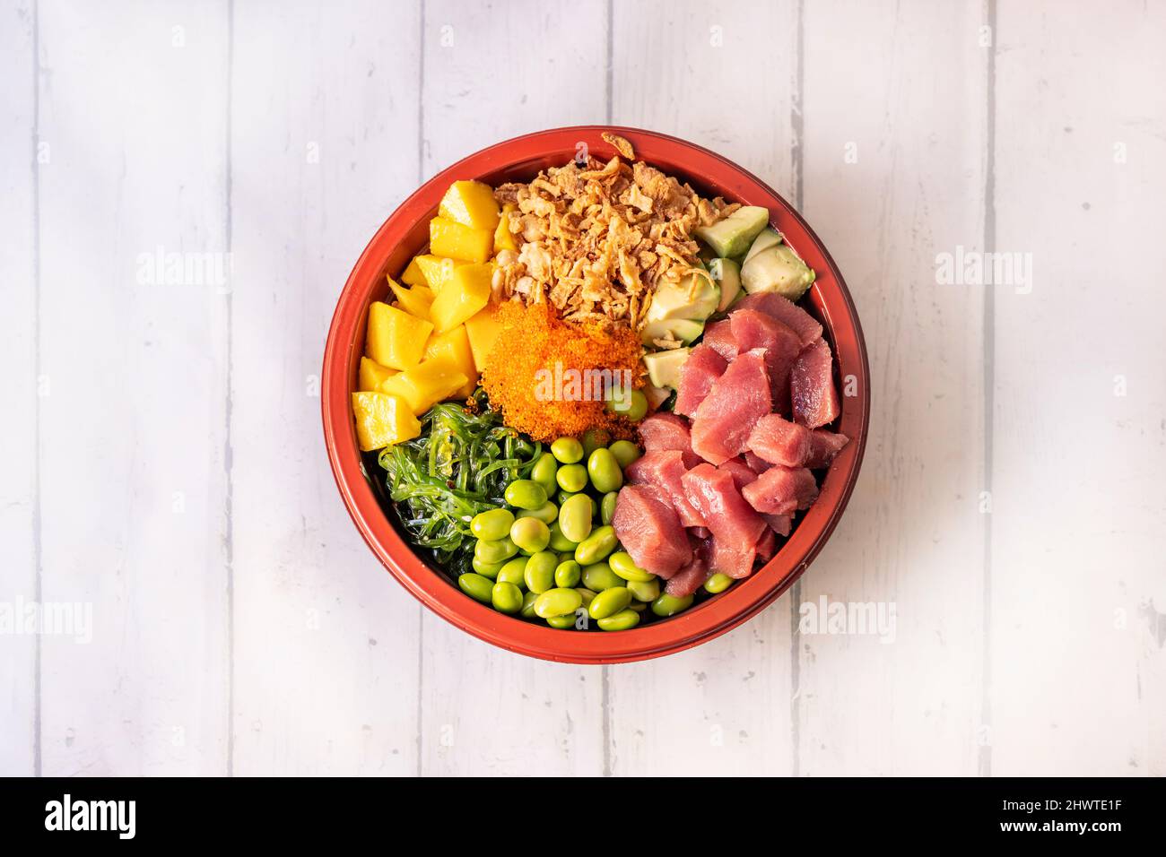 Grande ciotola di poke di tonno rosso tritato con mango, uova di masago, fagioli di edamame, alghe di wakame, avocado, riso bianco e cipolla croccante Foto Stock