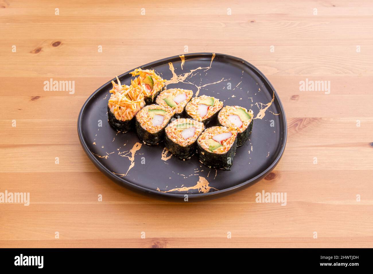 Maki spessi farciti con avocado, riso rosso e surimi su un tavolo di legno di pino Foto Stock
