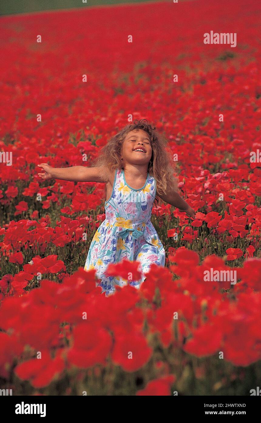 Gioiosa bambina che balla in campo pieno di papaveri, estate, radente, isola di Wight, Inghilterra Foto Stock