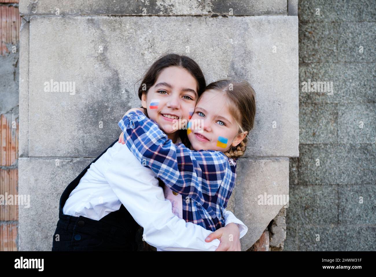 Ritratto di due bambine che abbracciano bandiere russe e ucraine sui volti. Concetto di pace, fermare la guerra e l'amicizia dei bambini contro Foto Stock