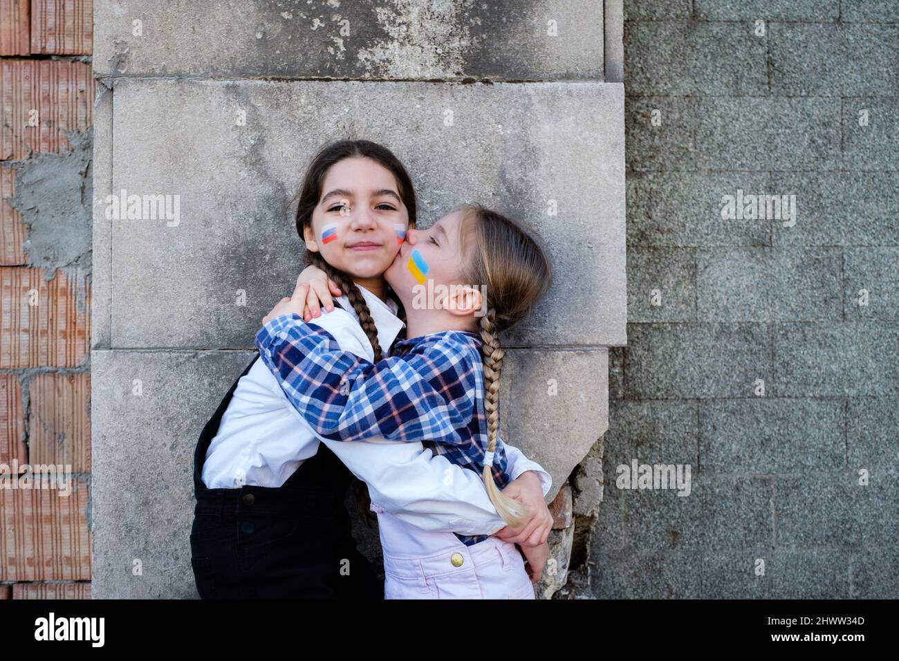 Ritratto di due bambine che abbracciano e baciano con bandiere russe e ucraine sui volti. Concetto di pace, fermare la guerra e l'amicizia del chi Foto Stock