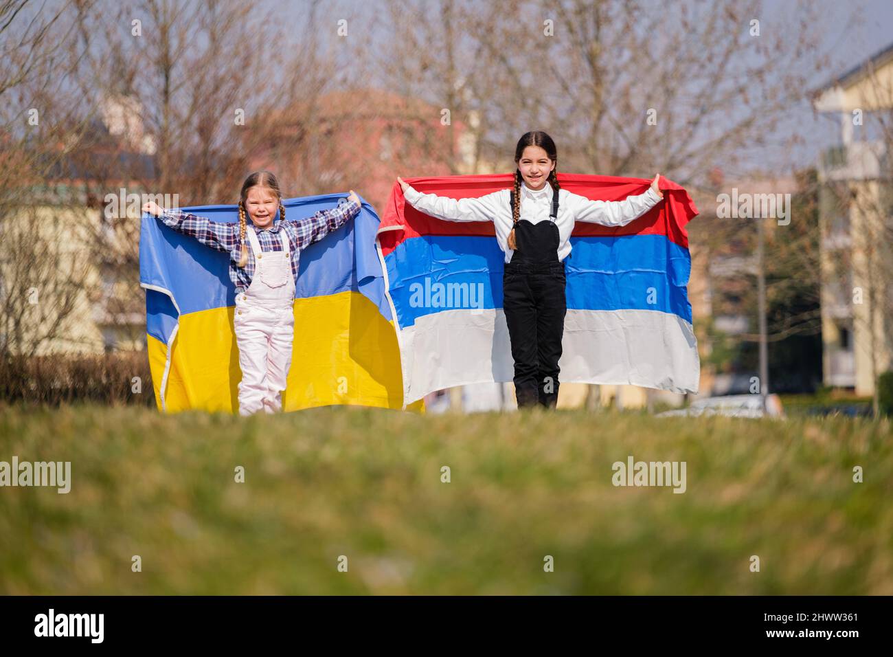 Belle bambine con bandiere ucraine e russe che corrono felici nel parco. Concetto di pace tra il popolo ucraino e russo Foto Stock