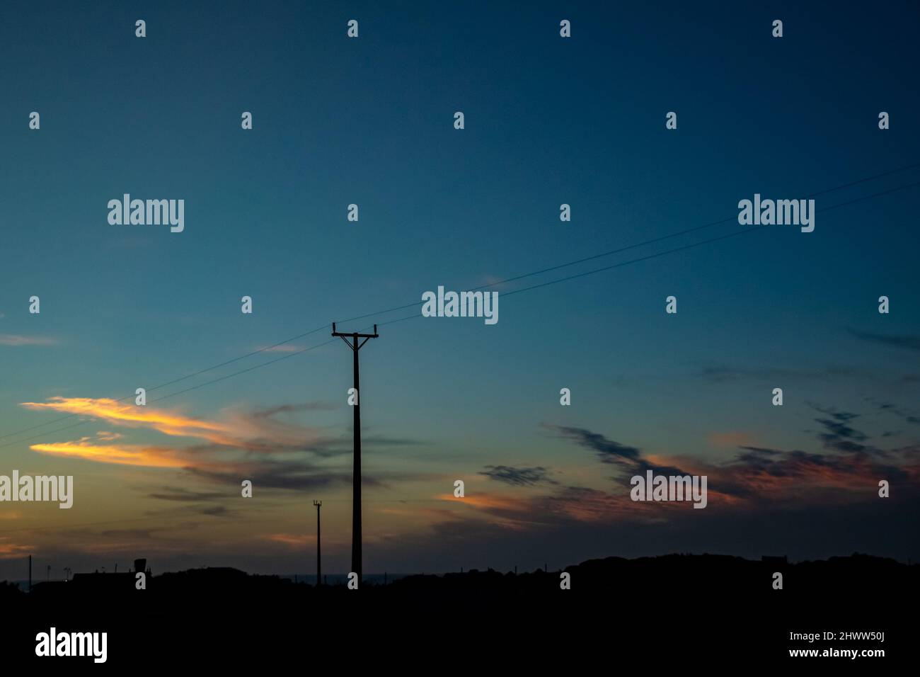 Le linee elettriche si silhoutes tra le ore dorate e blu Foto Stock