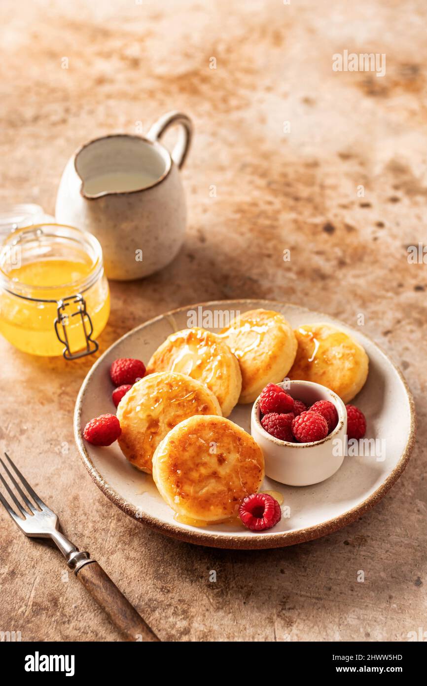 Pancake al formaggio casolare, sciroppi con miele e lampone fresco su sfondo testurizzato Foto Stock