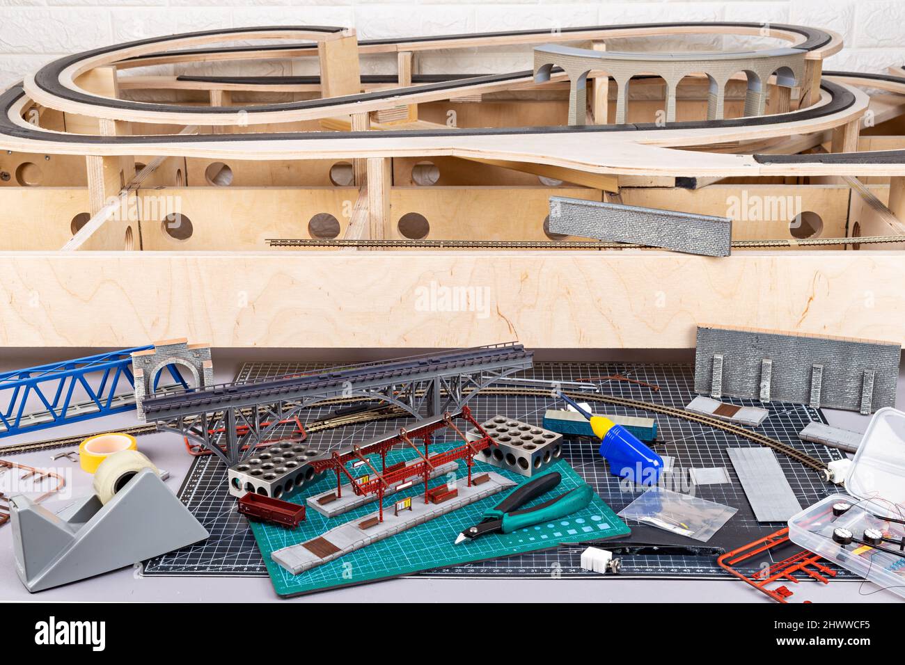 costruzione di una ferrovia modello con struttura in legno aperta. banco da lavoro con stazione ferroviaria modello e attrezzi per il paesaggio. scala per il tempo libero hobby mo Foto Stock