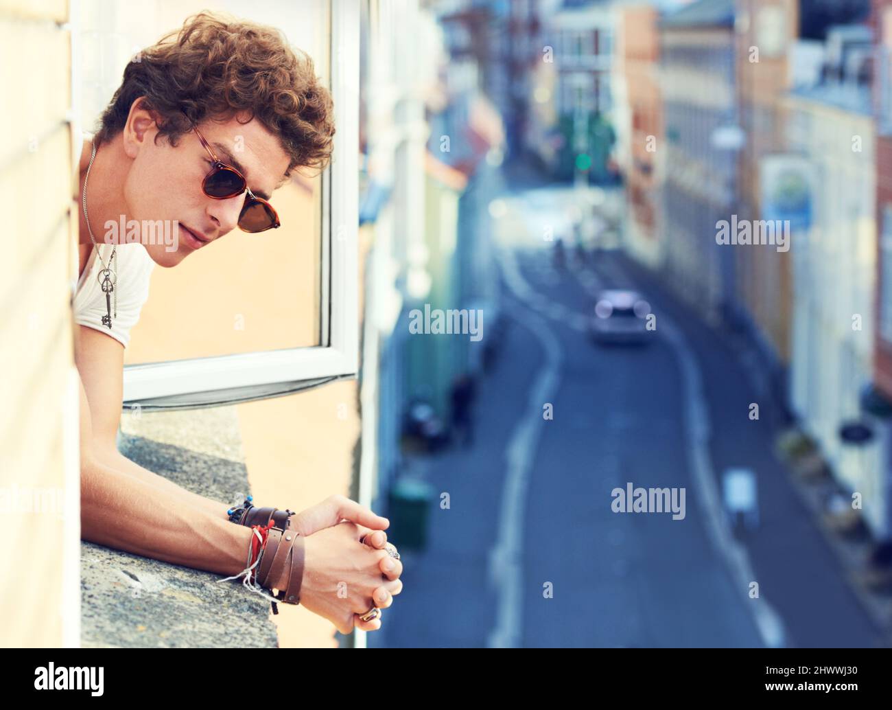 Solo un osservatore casuale. Un giovane che guarda la strada molto sotto mentre si alleva da una finestra. Foto Stock