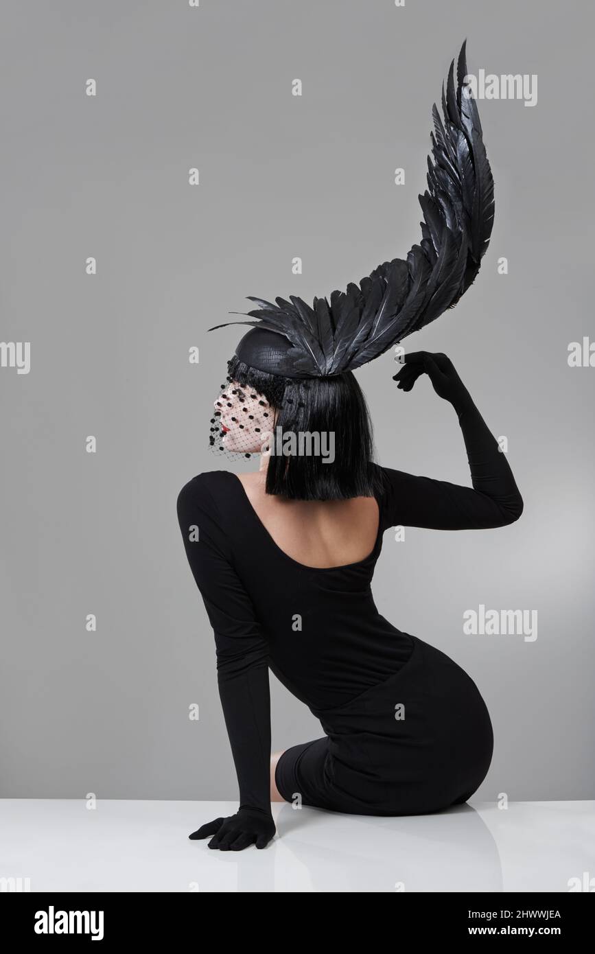 Moda sfumata. Scatto di una giovane donna in un headpiece a forma di ala seduto in uno studio. Foto Stock