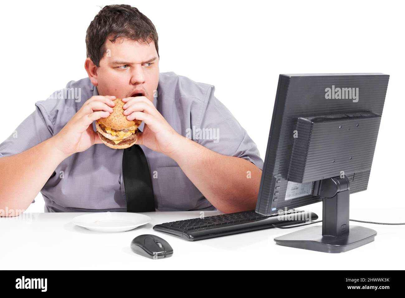 Smetta di mostrarmi cose sane. Un giovane uomo che mangia il suo pranzo alla sua scrivania al lavoro mentre fissava con la bocca agape al suo monitor - cibo malsano Foto Stock