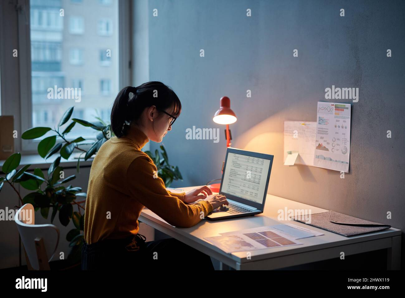 Giovane donna d'affari seduta sul suo posto di lavoro e lavorando con il progetto online utilizzando il laptop, lavora fino a tardi in ufficio Foto Stock