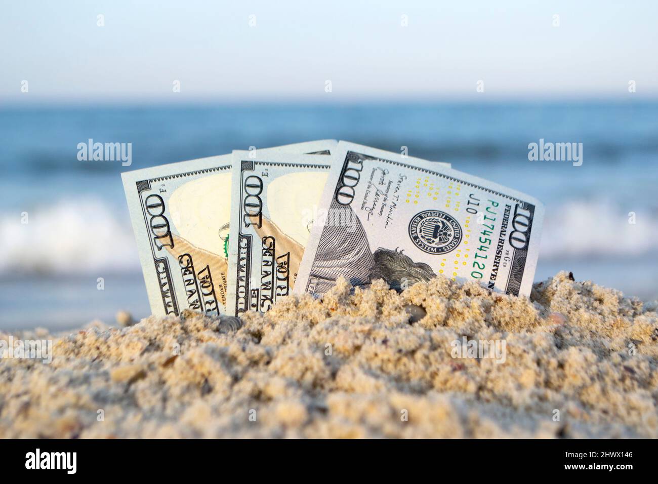 Trecento dollari bollette mezzo sepolto in sabbia su sabbia sabbiosa spiaggia primo piano Foto Stock