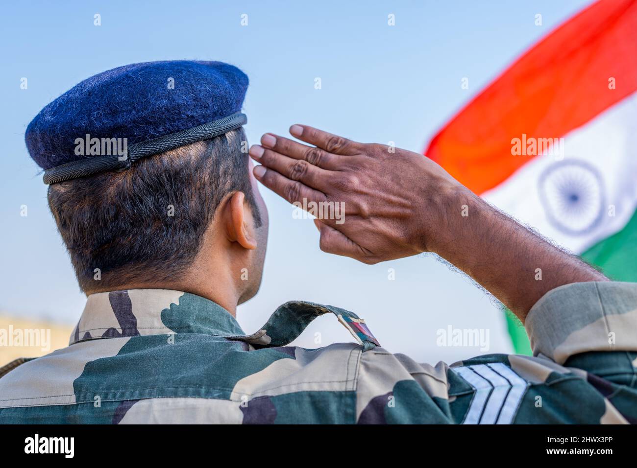 Back view shot di orgoglioso militare indiano saluta osservando bandiera indiana - concetto di patriota, nazionalismo e onore Foto Stock