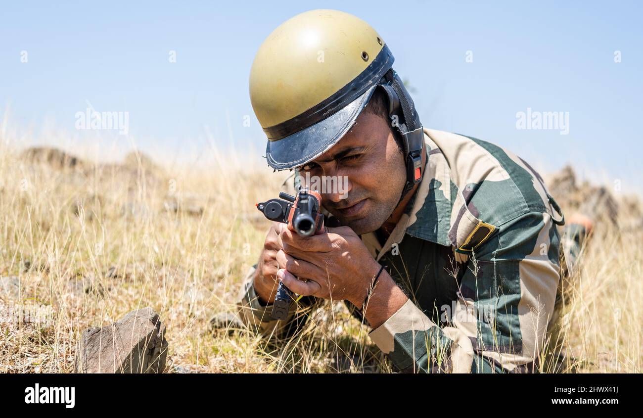 Solider dell'esercito con pistola che mira al bersaglio mentre si abbatte behinf le pietre di roccia sulla cima della collina - concetto di tattiche di guerra, combattimento e sorveglianza Foto Stock